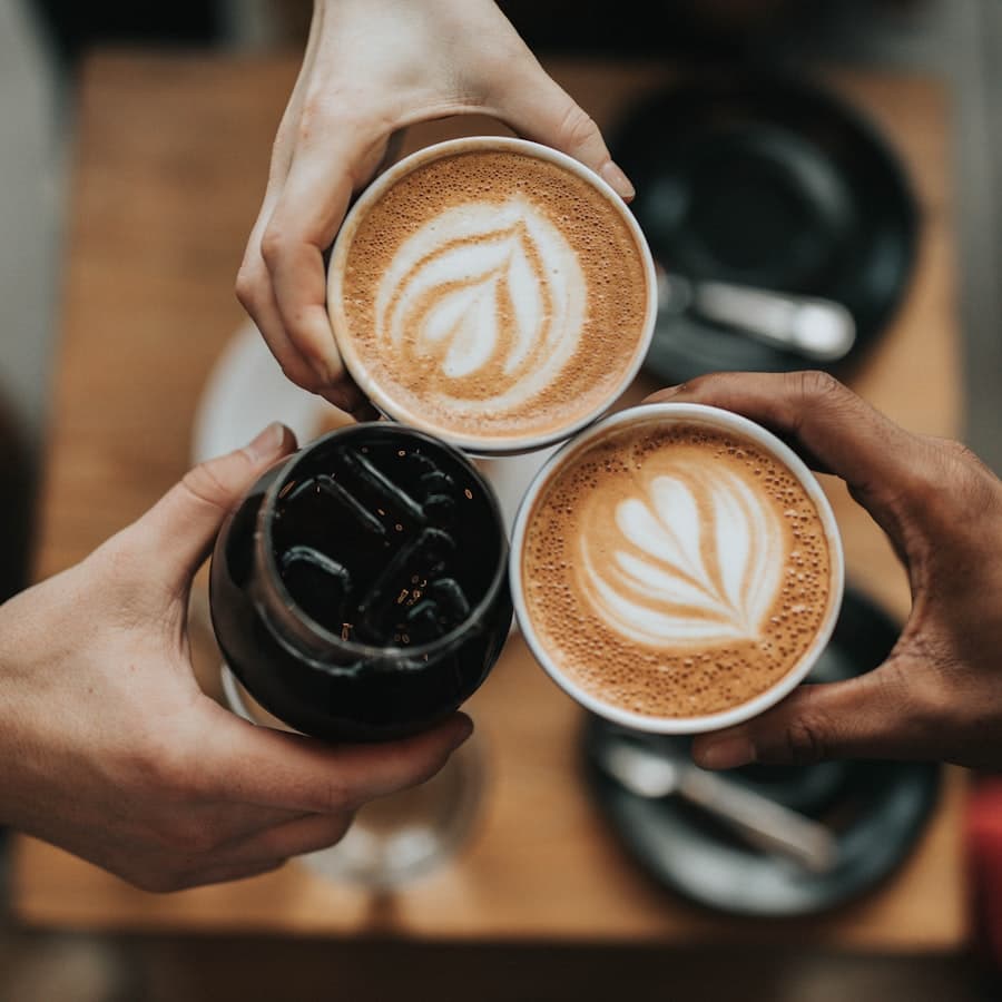 Three hands holding lattes with rosetta art, seen from above